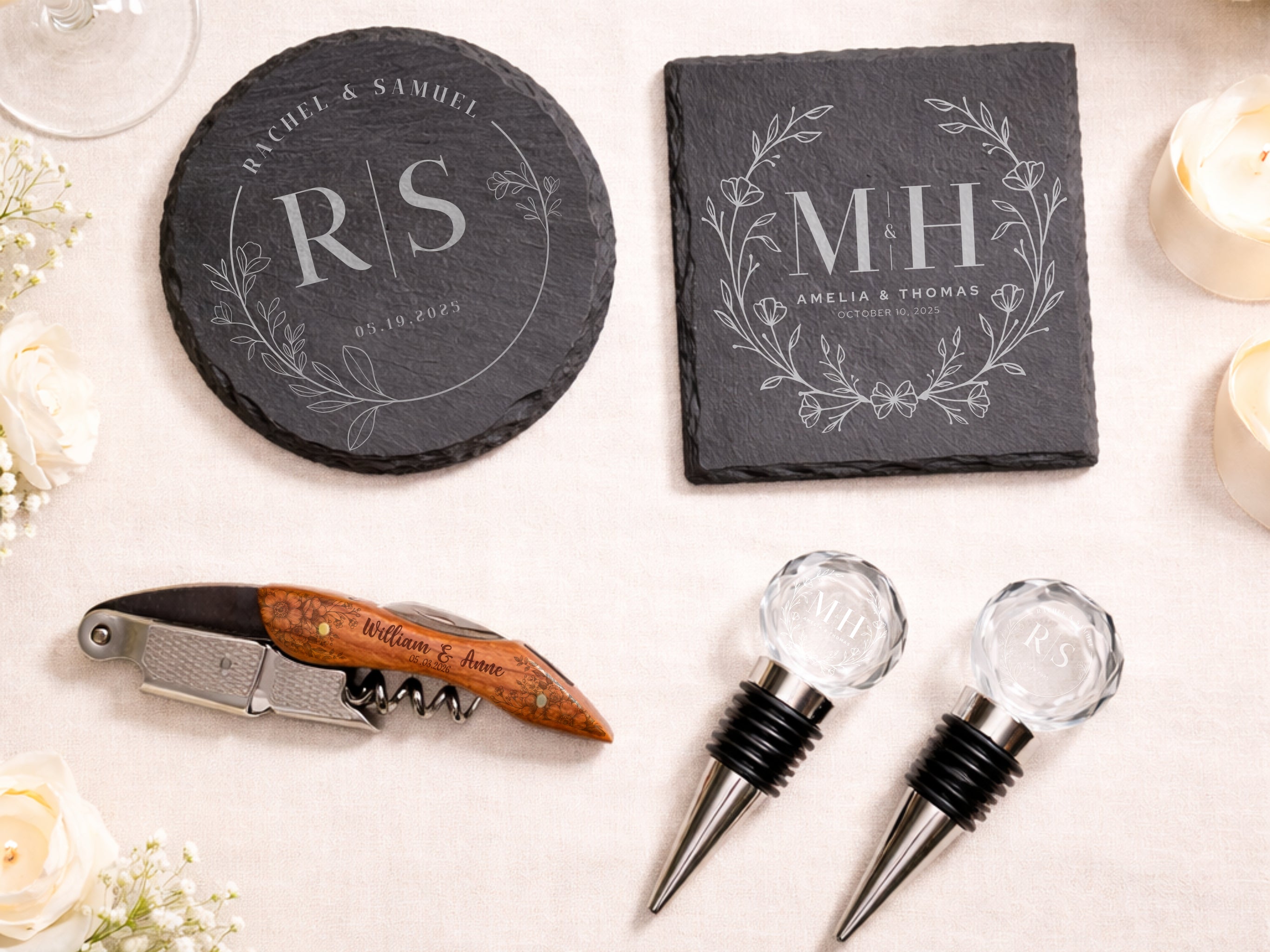 Personalized slate coasters and wine accessories arranged on a light fabric surface with flowers. 