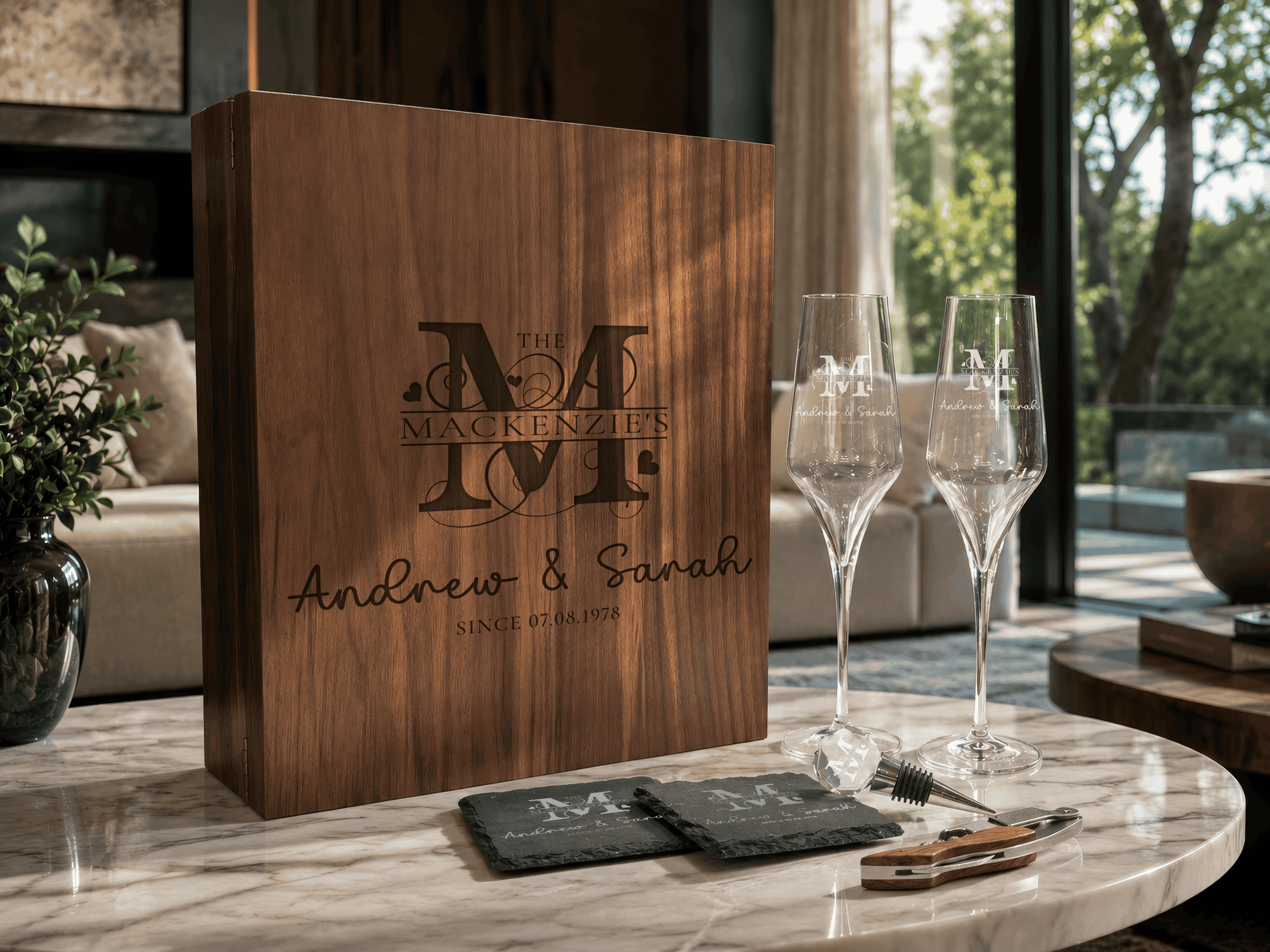 Wooden box with engraved initials and names on a table with glasses and coasters.