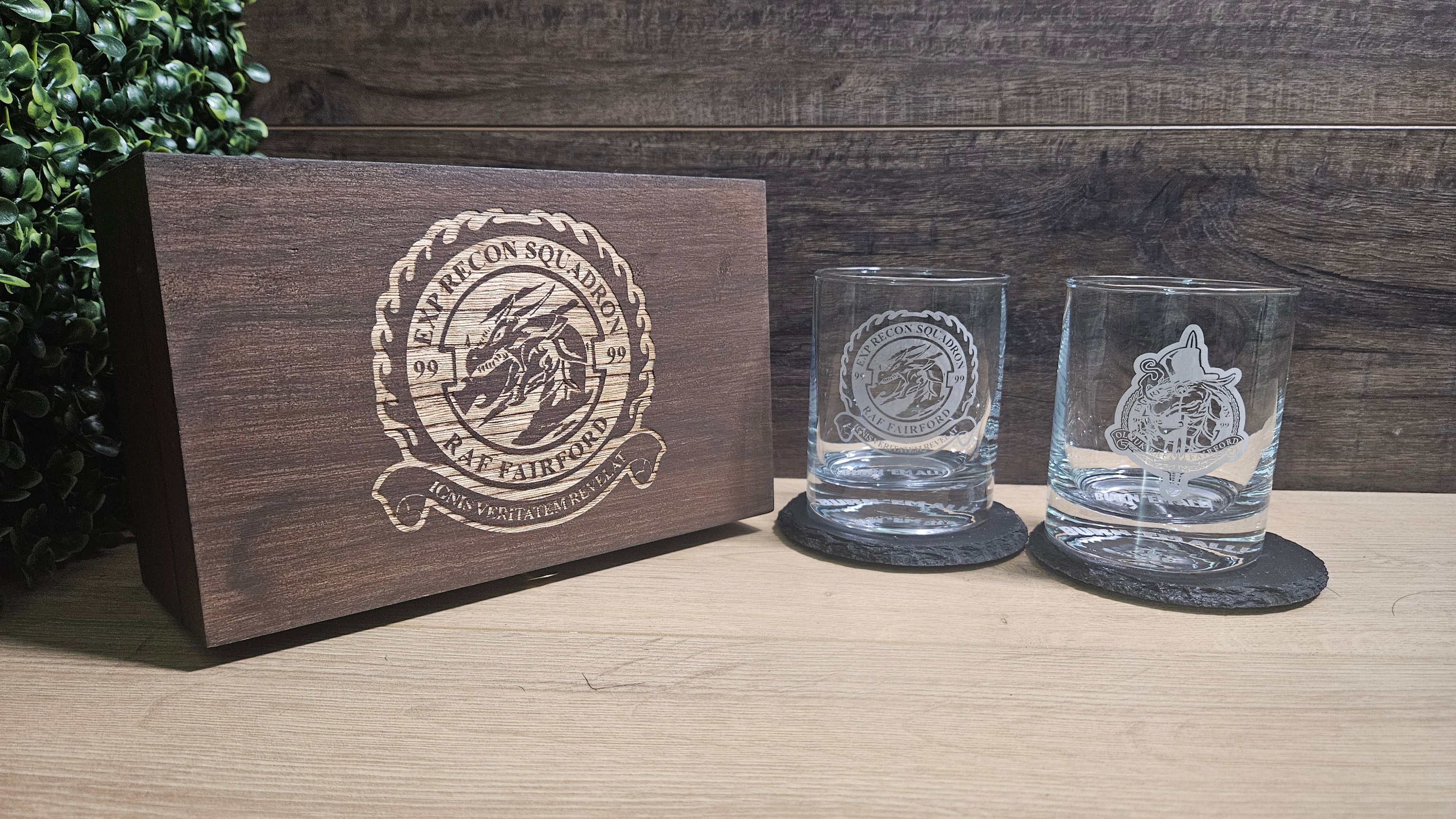 Two engraved glass tumblers with a wooden box featuring a logo on a wooden surface.