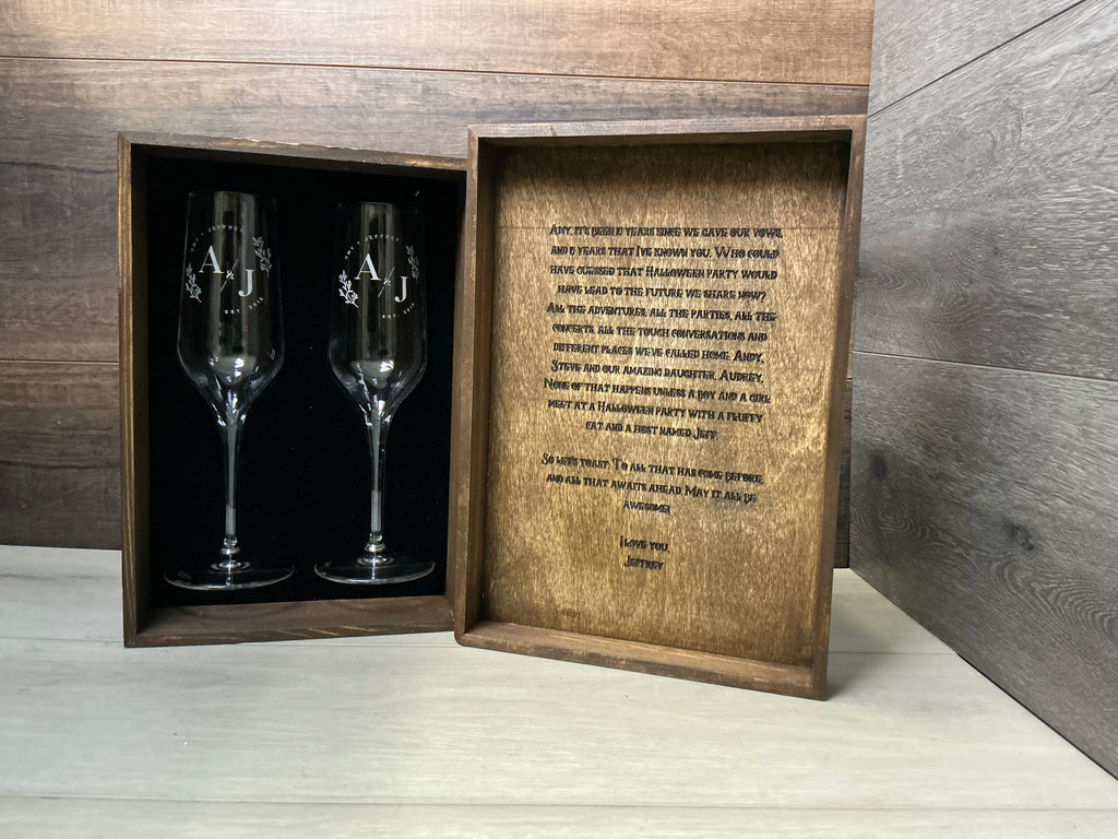 Wooden box with engraved text and two Champagne glasses inside, on a wooden Box.