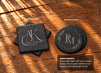 Two engraved slate coasters are displayed on a wooden tabletop: a square coaster on the left and a round coaster on the right. The coasters are dark charcoal gray with light engraved lettering and decorative flourishes.
