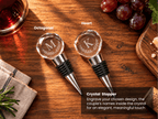 Two personalized crystal wine stoppers with engraved monogram letters 'M' and 'K' on faceted round tops, shown on a wooden tabletop with grapes, a glass of red wine, and a cutting board. Text labels identify the shapes as Octagonal and Heart, with a product description box at the bottom right.