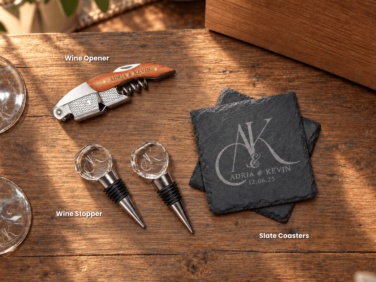 Personalized wine accessories set on a wooden table, including a corkscrew wine opener with an orange handle, two clear crystal wine stoppers with black rubber seals, and a stack of dark slate coasters engraved with a monogram and the names 'ADRIA & KEVIN'.
