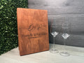 Wooden menu cover with engraved text and two champagne glasses on a wooden surface.